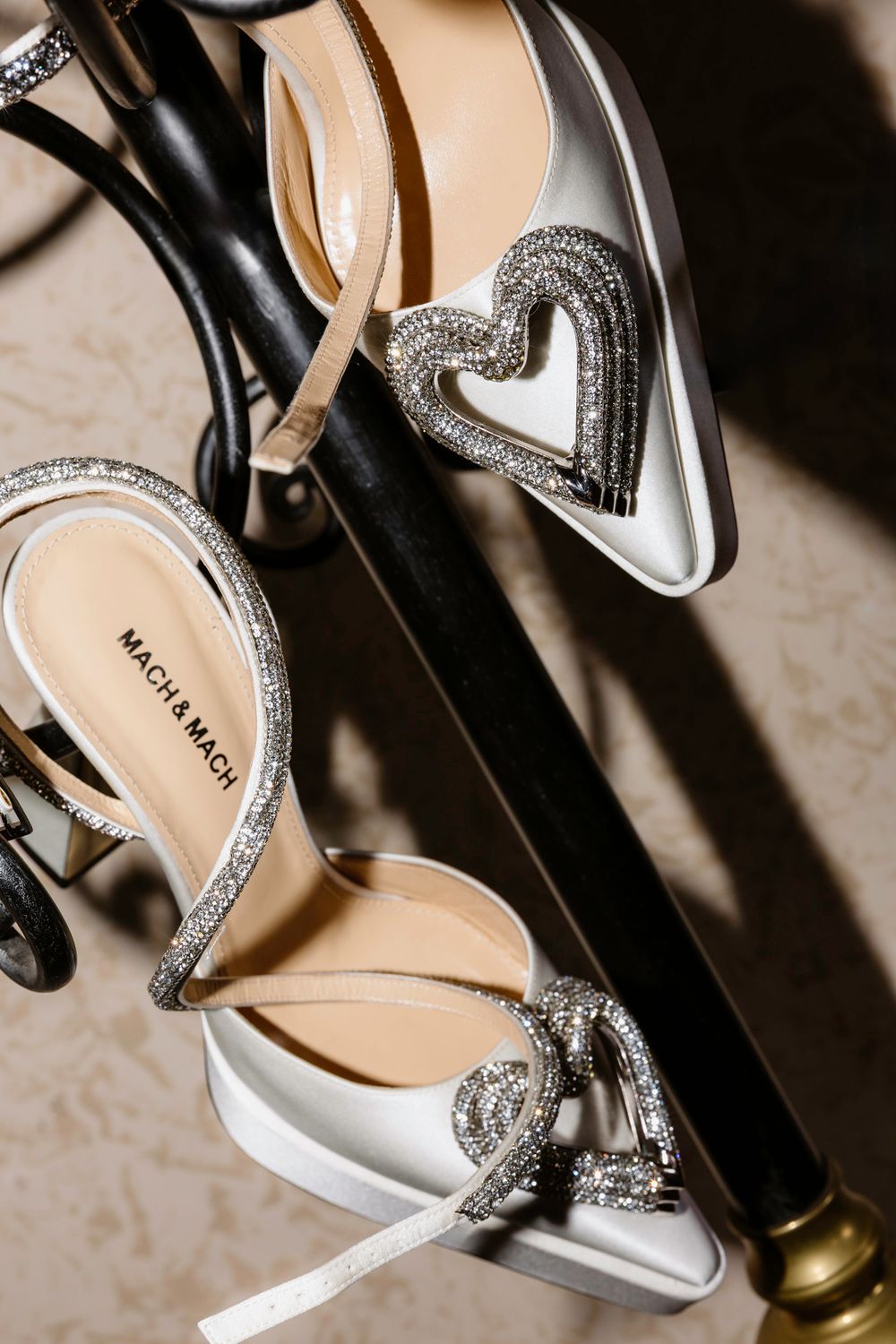 Elegant white bridal shoes with crystal heart embellishments and silver detailing rest against a dark surface.