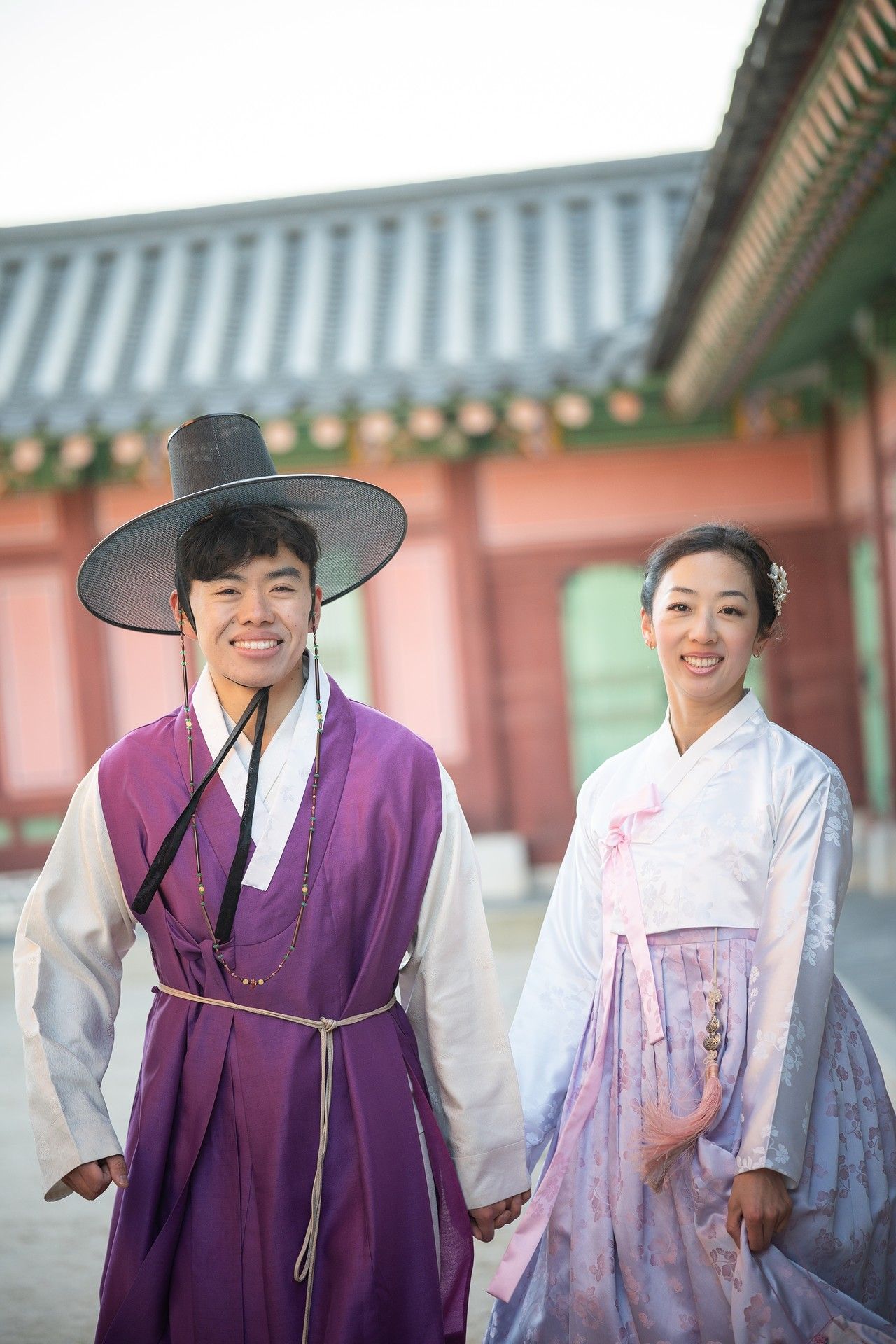 People wearing traditional Korean hanbok clothing in purple and white stand together at a historic palace courtyard.
