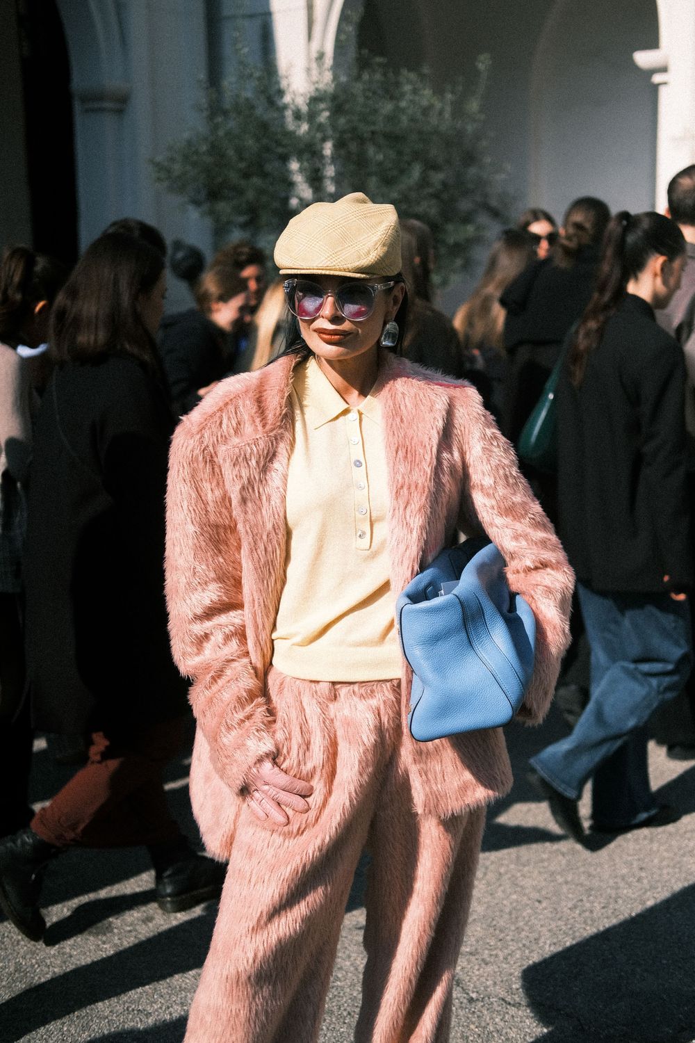 A person wearing a pink fuzzy coat and baseball cap poses in four similar street style fashion shots.