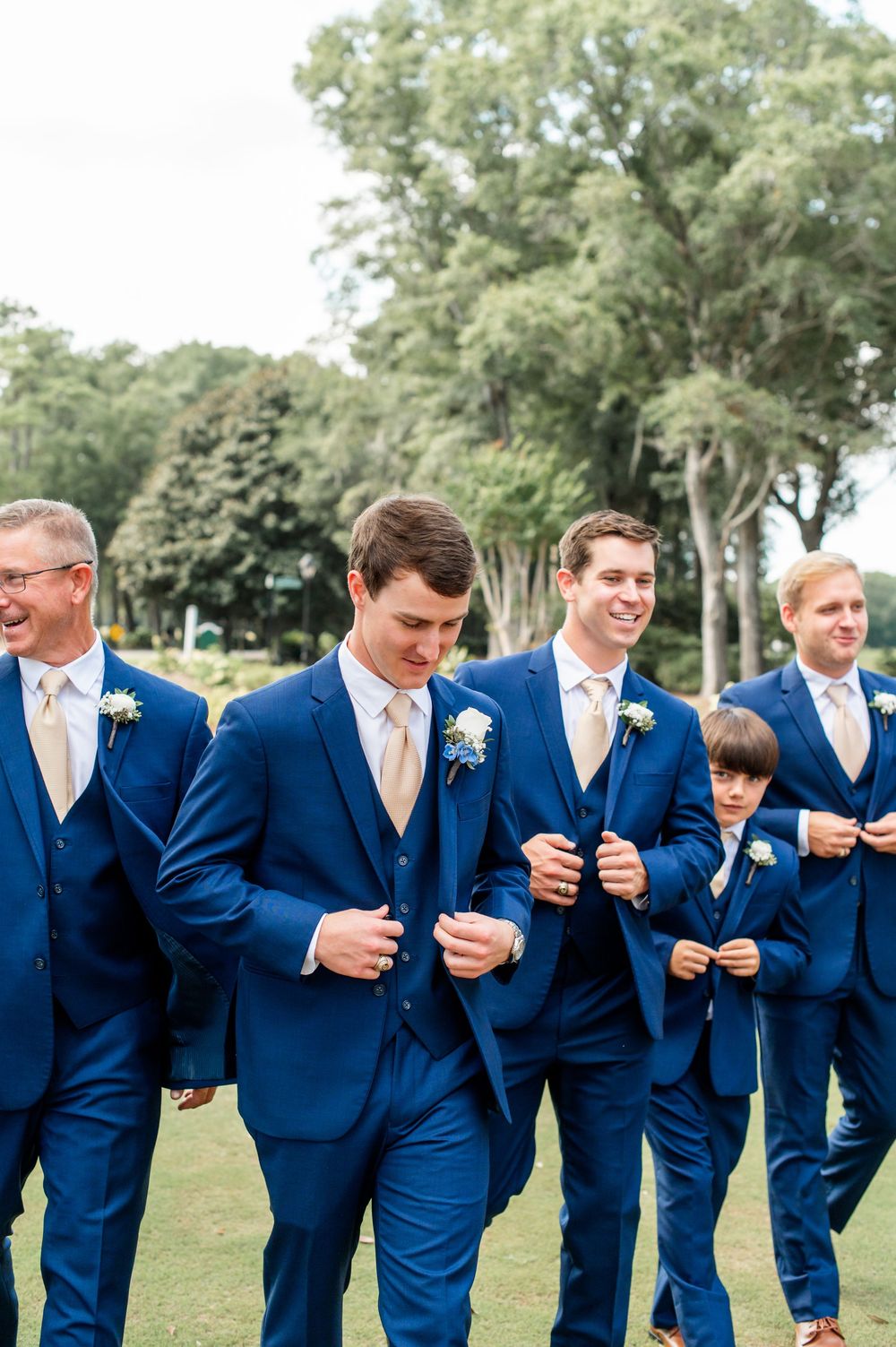 Groomsmen in navy suits share laughs during casual outdoor photo session.