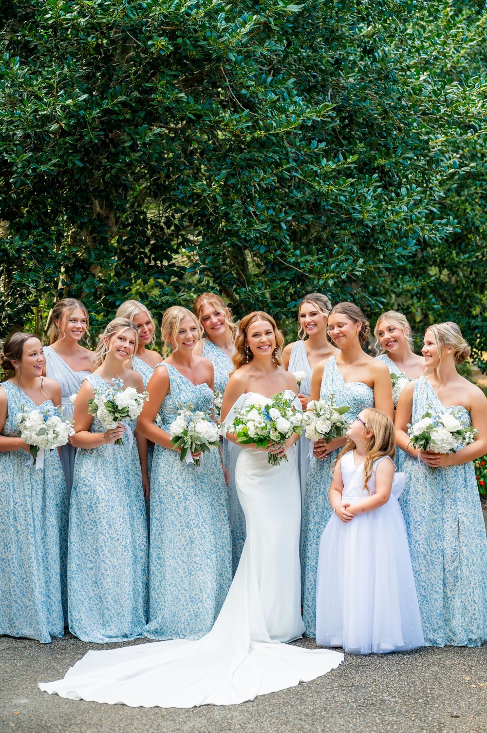 Bridesmaids in light blue sequined dresses pose together holding white bouquets against a green garden backdrop.