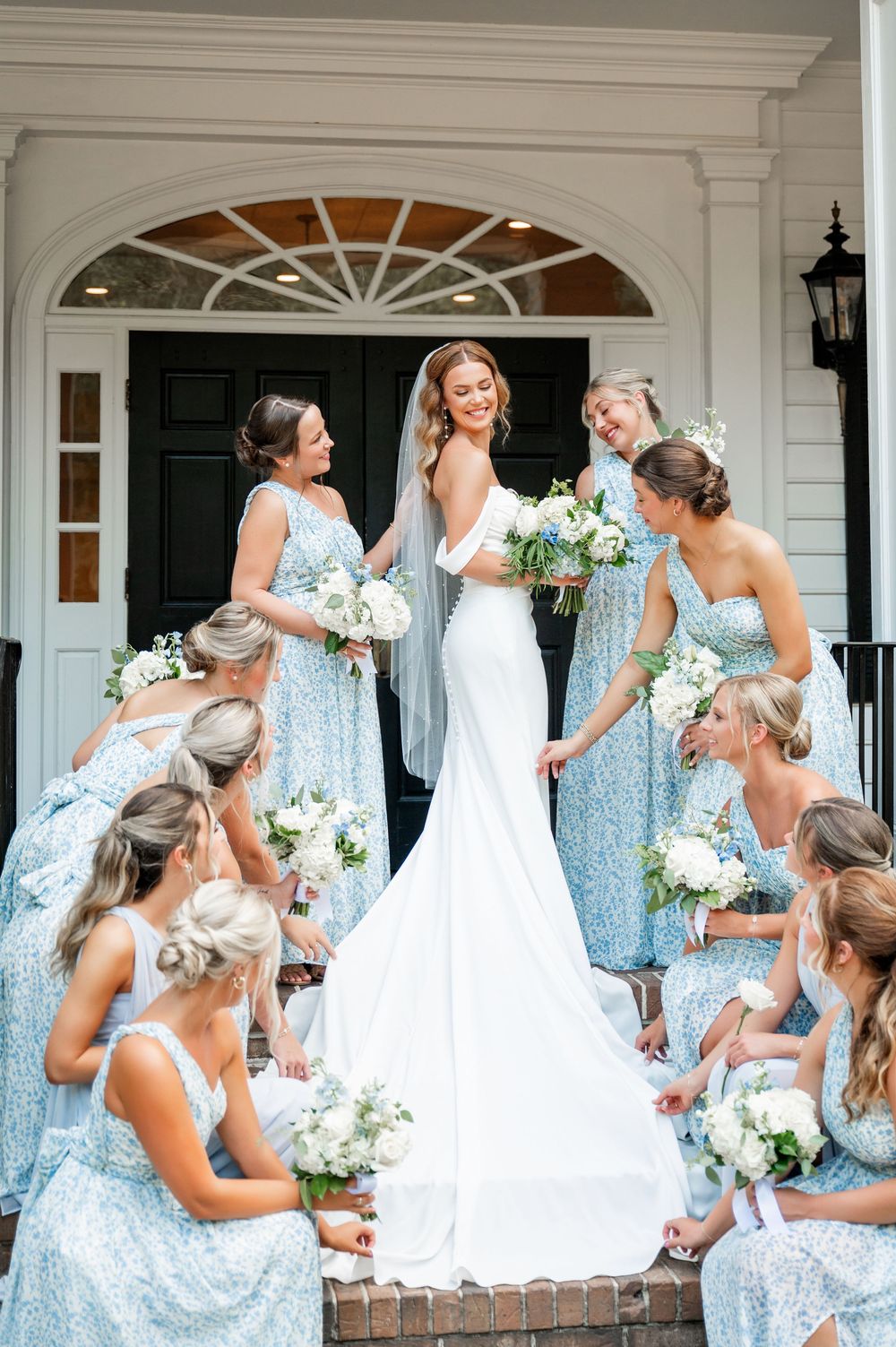 Bridal party shares joyful moments on a white columned porch wearing light blue sequined dresses.