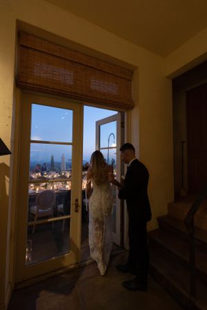 Silhouetted figures in formal attire standing by window with city view at dusk.
