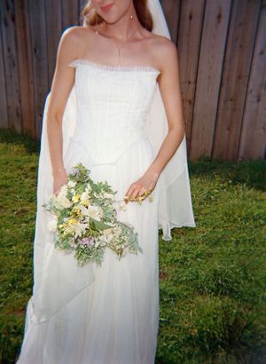 A strapless white wedding dress and delicate bouquet of cream and green flowers stand out against a wooden fence backdrop.