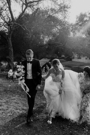A black and white wedding photo showing a couple walking together on a tree-lined path.