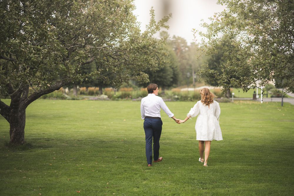 Couple holds hands while walking through a lush green park on a sunny afternoon.