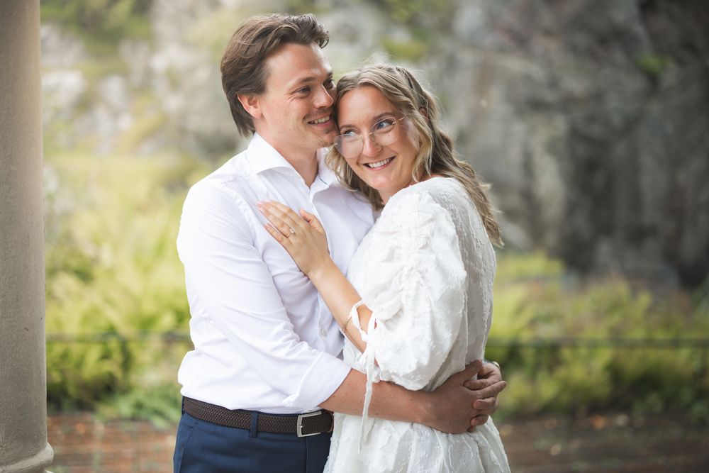 A romantic couple in white outfits embraces during an outdoor photo session with soft natural lighting.