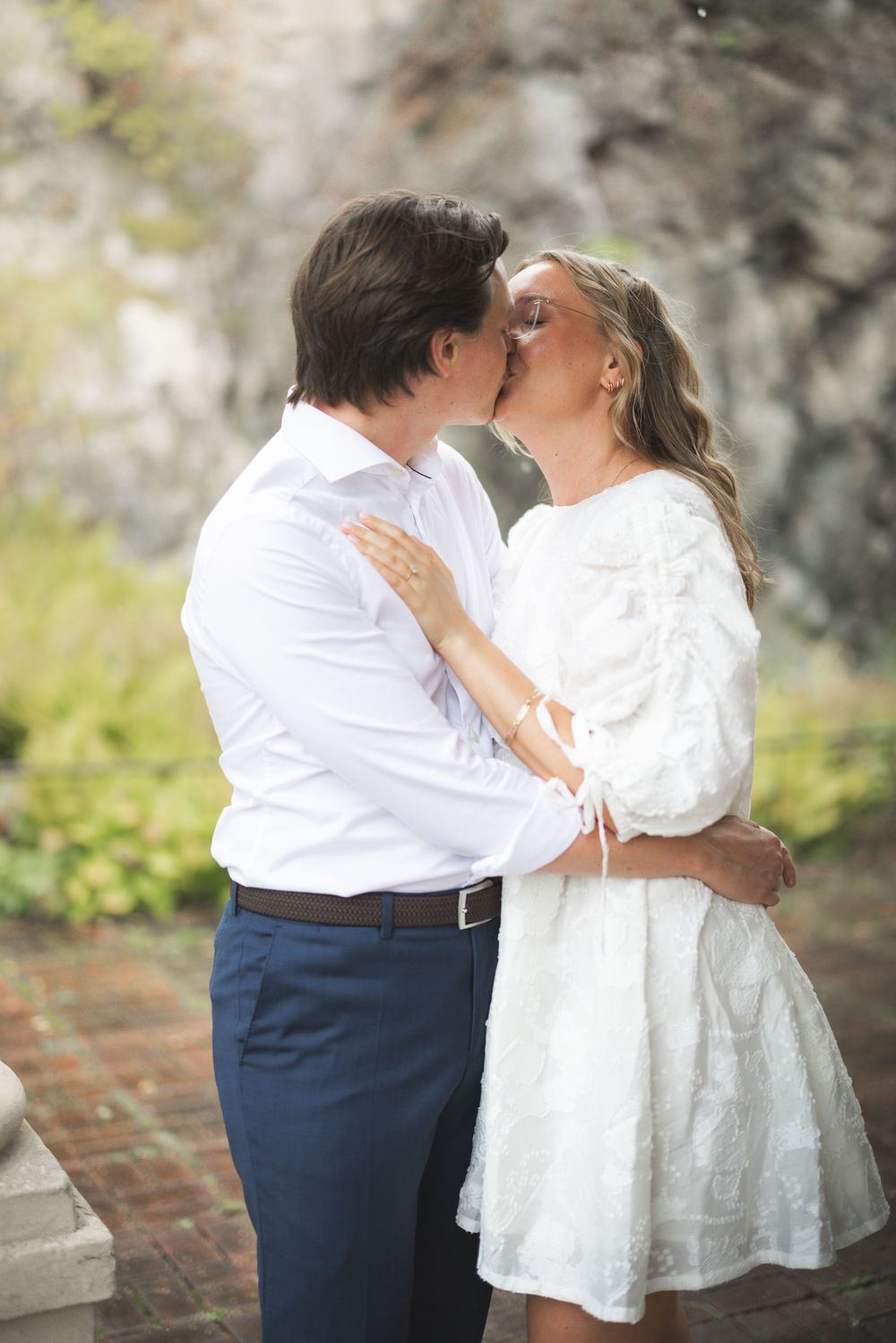 A romantic couple shares tender kisses in a series of photos wearing white and navy blue formal attire.