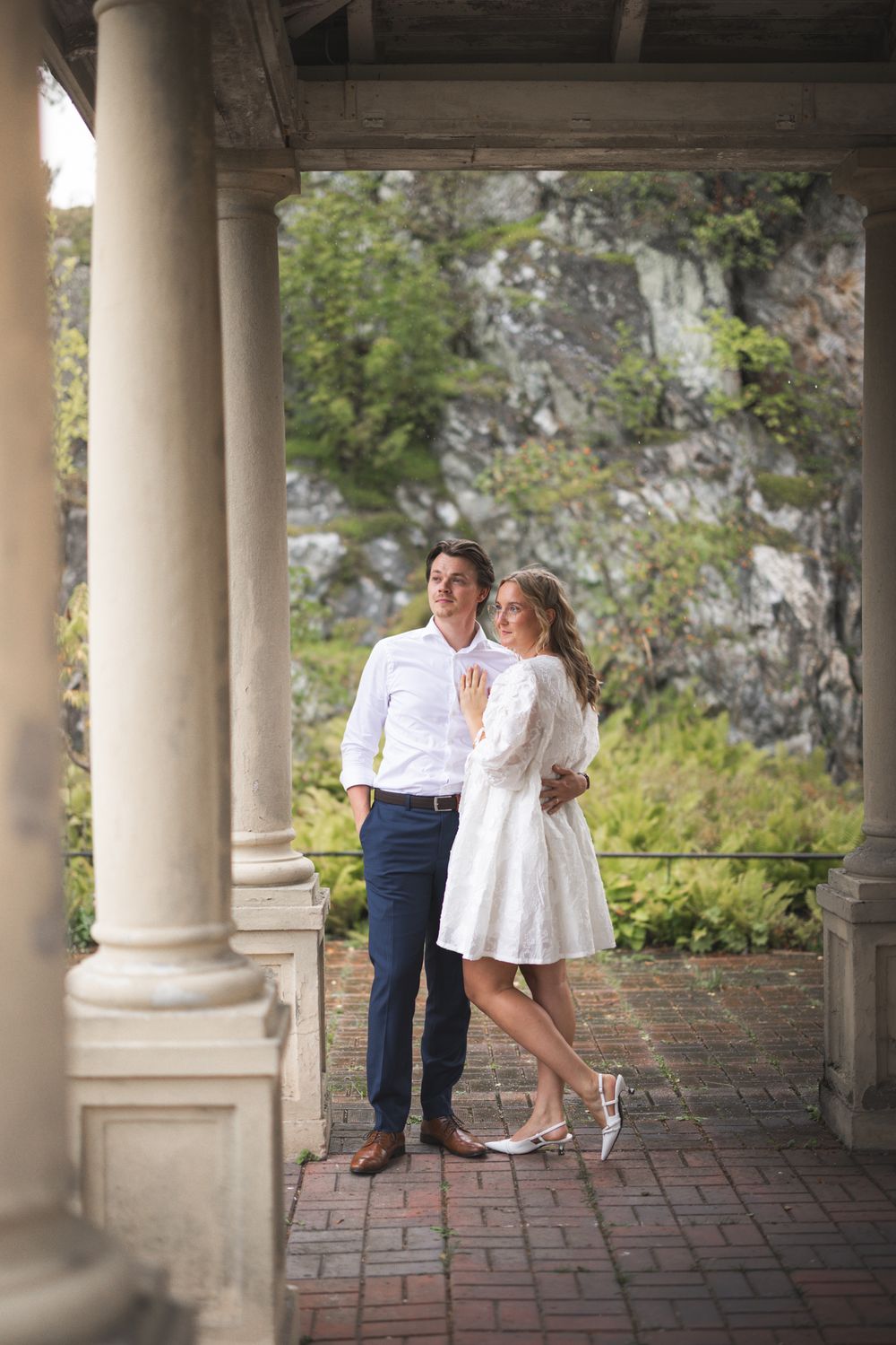 Romantic couple shares tender moments in an elegant colonnade with stone pillars and natural light.