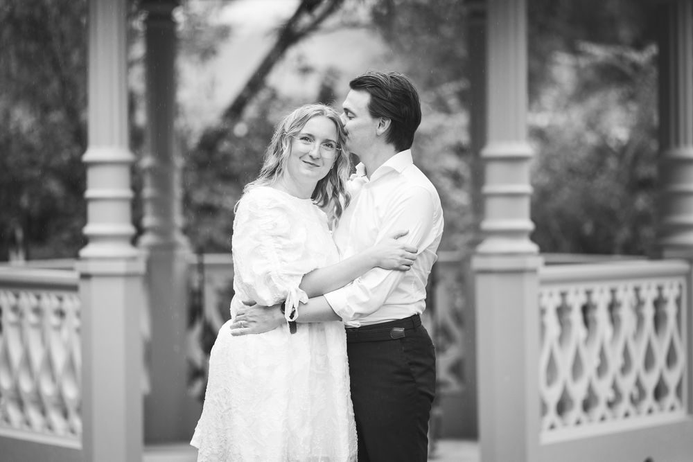 A romantic couple embraces outdoors in a series of black and white photos with white railings and columns in the background.