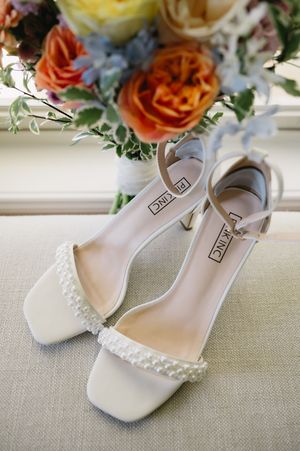 Elegant white bridal shoes with pearl details and floral decor displayed against a light background.