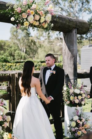 Outdoor wedding ceremony with rustic wooden arch decorated in pink and peach floral arrangements.