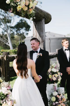 Intimate outdoor wedding ceremony with floral decorations and rustic wooden fence backdrop.