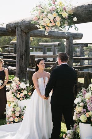 Wedding couple standing under rustic wooden pergola decorated with pastel flowers.