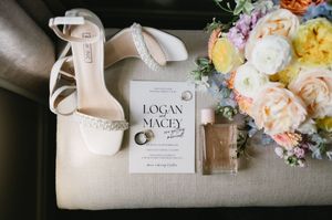 Wedding details including elegant bridal shoes, floral arrangements, and personalized name cards arranged on light fabric.