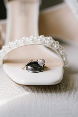 Wedding rings and diamond engagement ring displayed on a white satin shoe with pearl details.