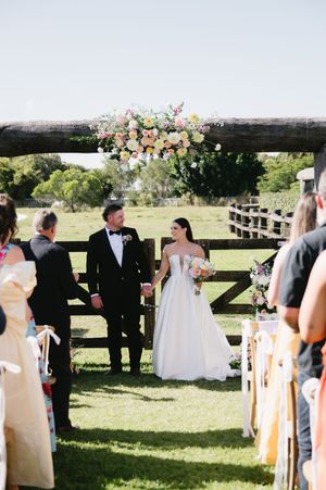 Outdoor wedding ceremony setup with white chairs and floral decorations on rustic wooden fence.