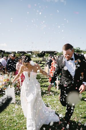 Wedding celebration with confetti flying through the air as guests celebrate on a green lawn.