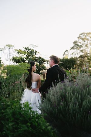 Wedding couple embracing in garden surrounded by lavender and greenery at sunset.