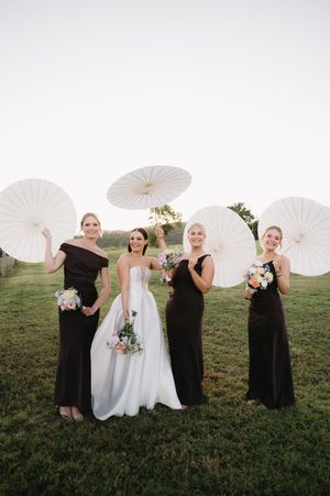 Wedding party poses on grass with white parasols and contrasting black and white dresses.