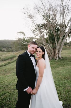 Newlyweds share intimate moment among gnarled trees on hillside.
