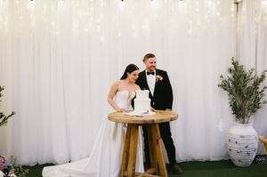 A couple cuts their wedding cake together at an elegant reception with white drapes and greenery decor.