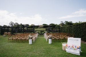 Rustic outdoor wedding ceremony setup with wooden chairs and white decorations in a grassy field.