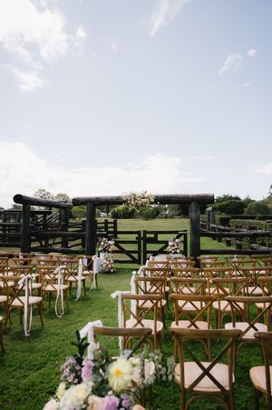 Wooden cross-back chairs set up for an outdoor wedding ceremony on a grassy lawn.