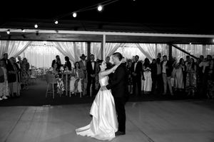 A couple shares their first dance at a wedding reception under a tent while guests watch from the perimeter.