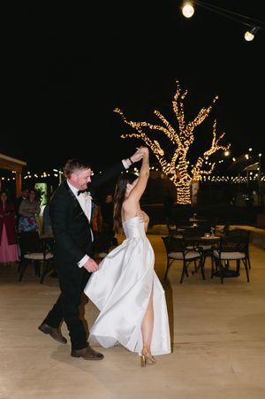 A couple dances together at an outdoor evening reception with string lights illuminating the background.
