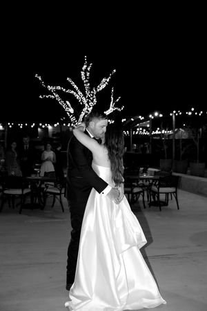 A couple dances together at an outdoor evening reception with twinkling lights decorating the trees.