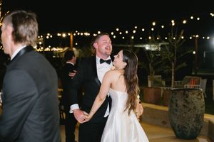 A couple shares a joyful moment while dancing at an outdoor evening wedding reception under string lights.