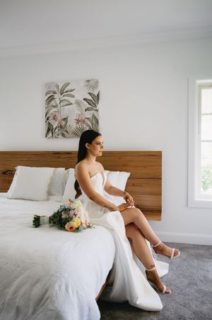Elegant wedding dress detail in a bright bedroom with wooden headboard and floral artwork on the wall.