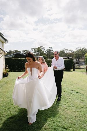Wedding party helping with a flowing white wedding dress on a sunny outdoor lawn.