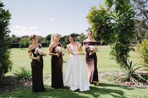 Wedding party poses together outdoors on a sunny day surrounded by lush green landscaping.