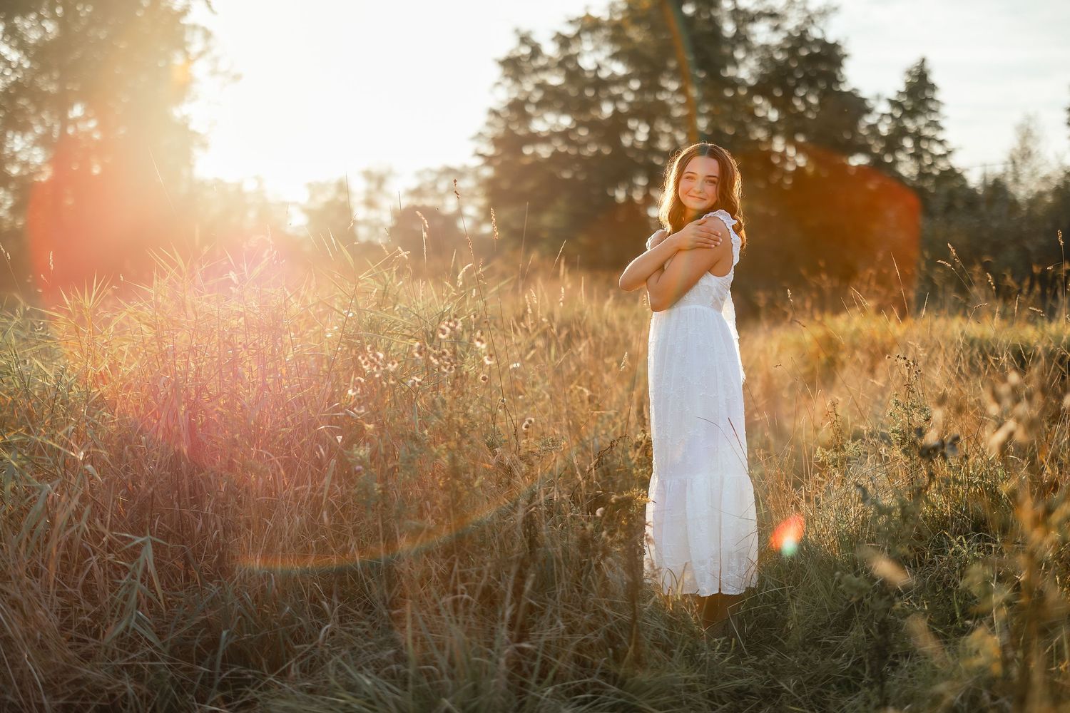 A white dress flows in a sunlit meadow during golden hour as sunflares dance through tall grass.