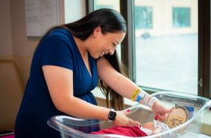 Person caring for infant in hospital bassinet wearing blue scrubs.