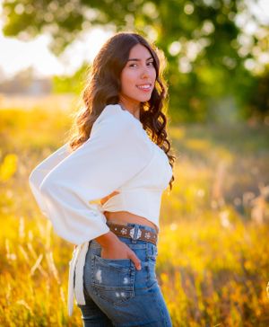 Portrait in white sweater and jeans against golden sunset in tall grass field.