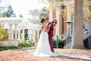 Wedding couple embracing outdoors near white pillars and autumn foliage.