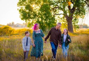 Family group walking together through a golden autumn field at sunset.