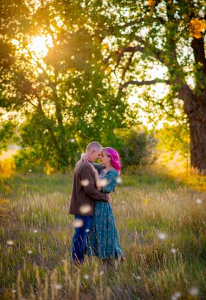 A romantic couple embraces in a sunlit meadow during golden hour with trees in the background.