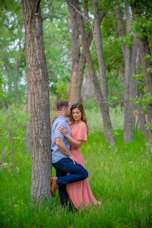 Playful couple's photoshoot in a serene wooded area with tall trees and green grass.