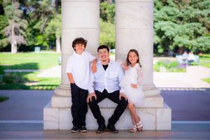 Three people sitting on white stone columns in casual attire.