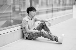 A casual portrait of someone sitting against a glass wall in black and white photography.