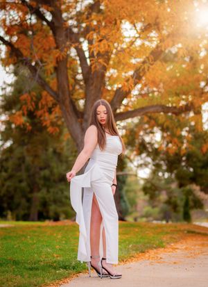 A figure in white poses on a path surrounded by autumn trees with golden leaves.