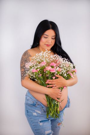 A person holding a beautiful bouquet of pink carnations and baby's breath against a grey background.