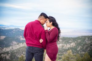 Couple in burgundy outfits sharing tender moments against a mountain backdrop.