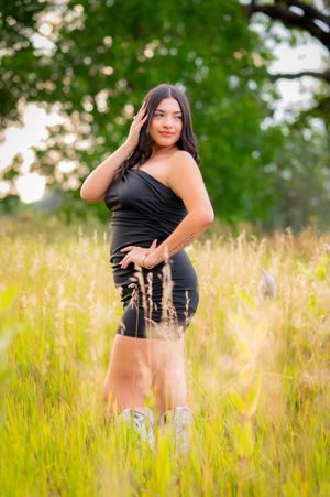 Portrait in tall grass field with soft golden sunlight and green trees in background.