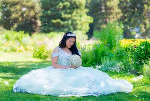 A figure in an elaborate white lace dress sits in a sunny garden setting.