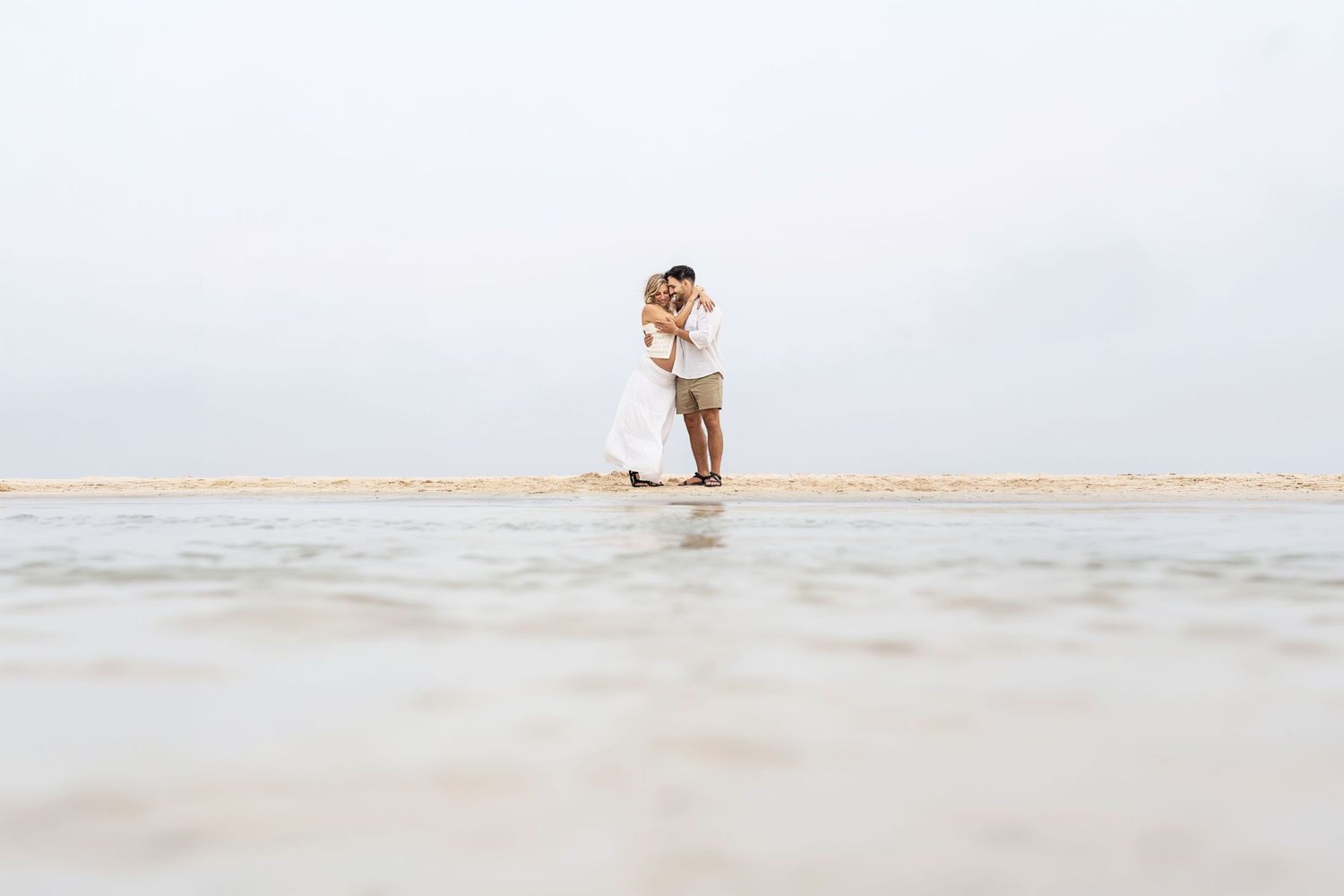 Expecting parents embracing on the shoreline during their maternity session at Esmeralda Beach in Playa del Carmen, Mexico.